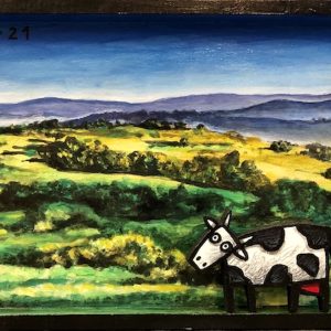 Vache stylisée en bois découpé placée devant un paysage peint de collines vertes, série Boîtes, 2021.