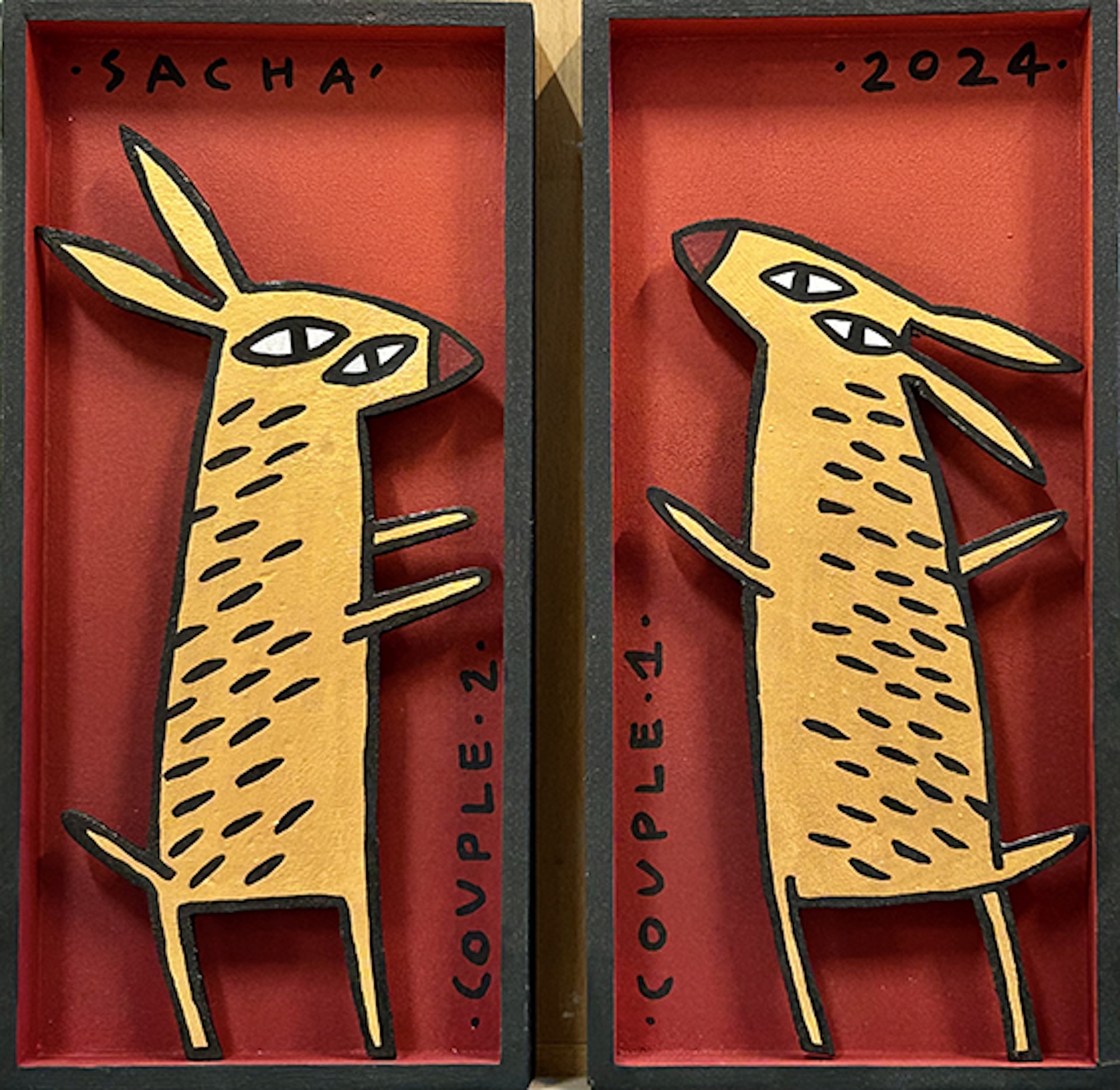 Deux figures animales stylisées en bois découpé représentant un couple de lapins, sur fond rouge avec inscriptions, présentées en diptyque dans la série Boîtes, 2024.